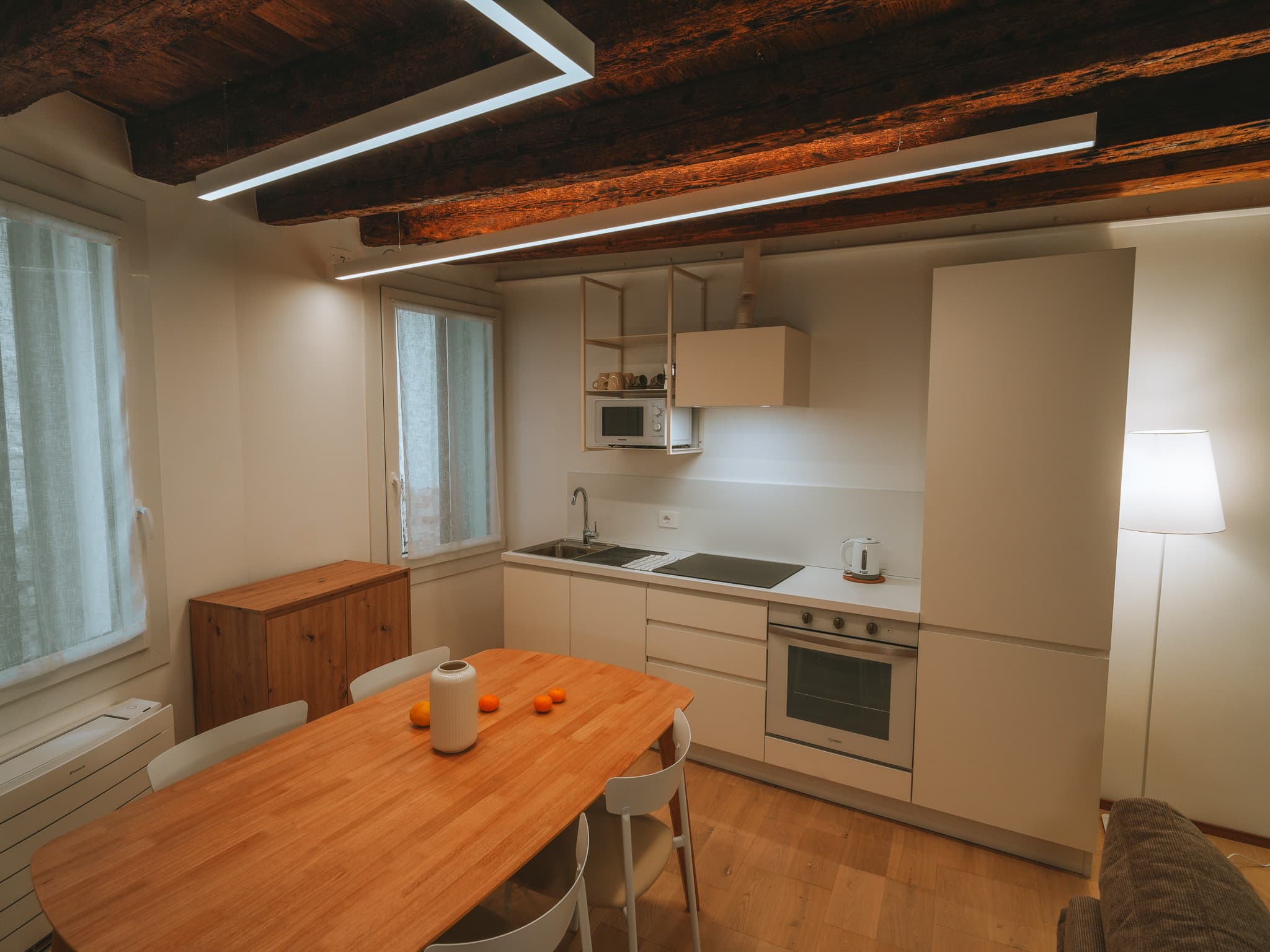 Angolo cottura bianco con lavello, forno e cappa, tavolo in legno con arance e vaso