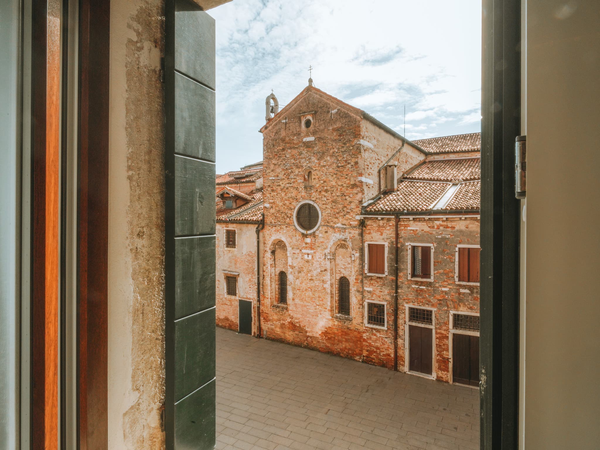 Chiesa in mattoni con rosone e campanile a vela vista da una finestra aperta