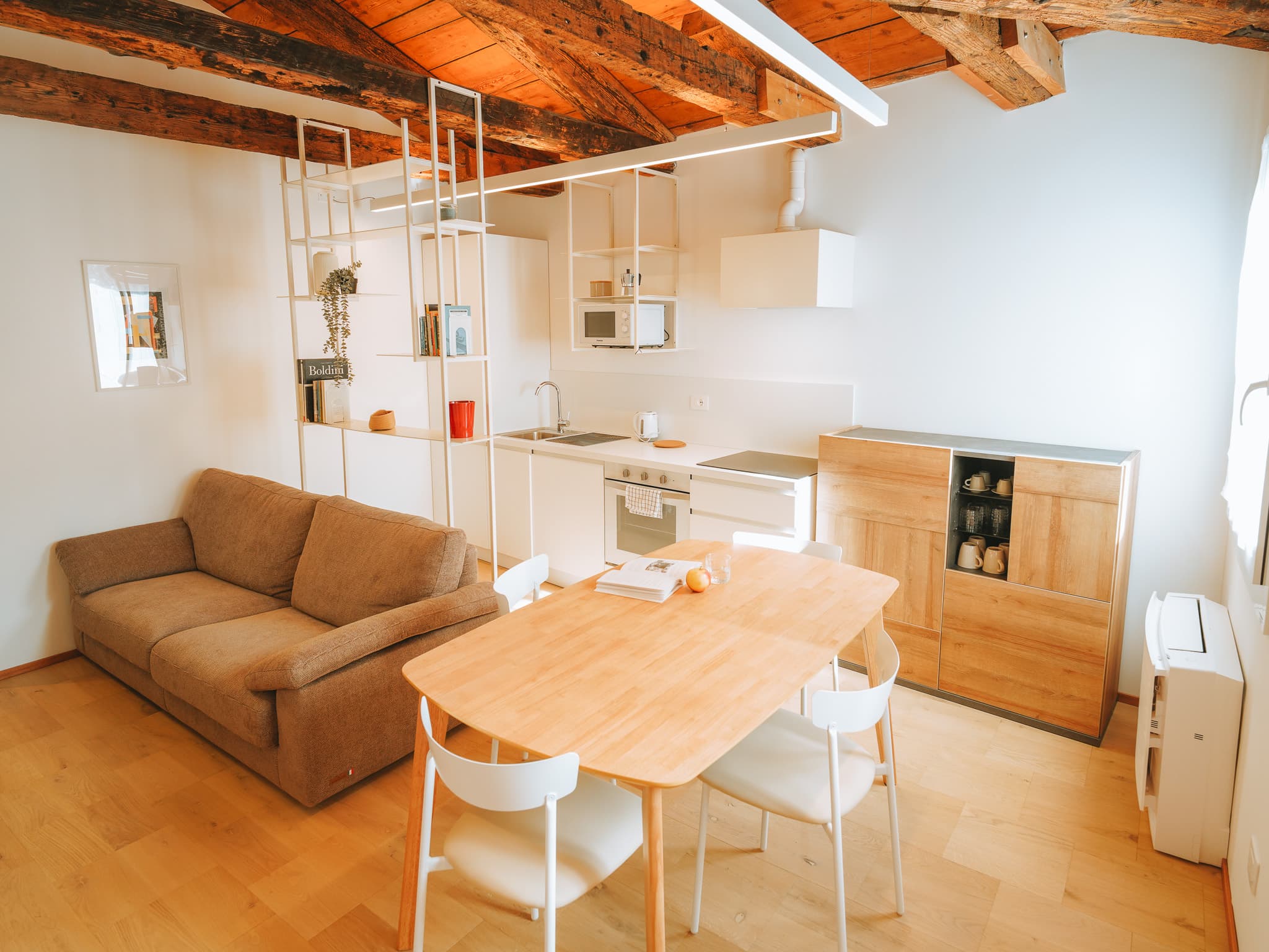 Divano, tavolo in legno e cucina bianca in un unico ambiente sotto travi a vista