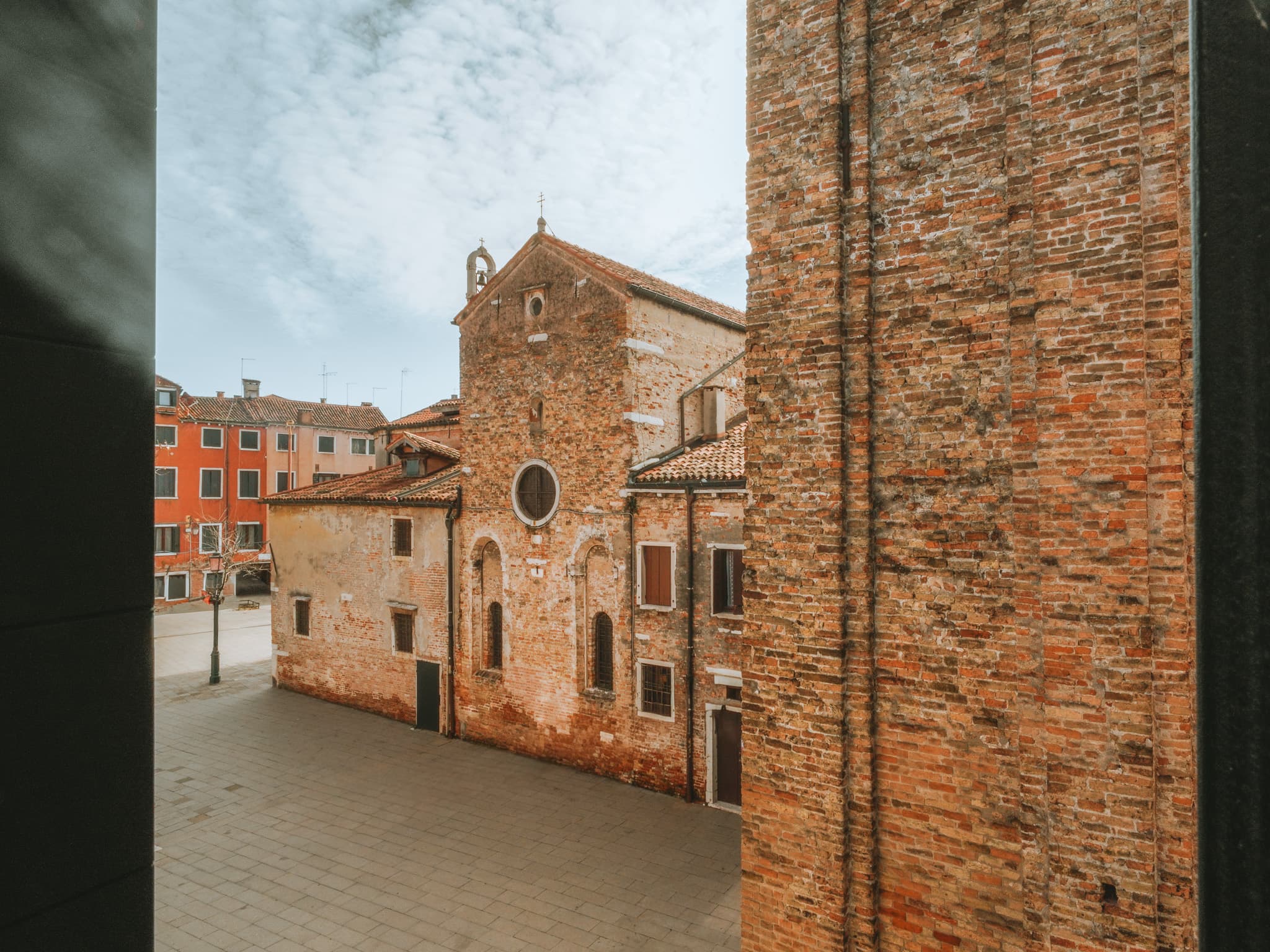 Chiesa in mattoni con rosone sul campo lastricato, case sullo sfondo, vista dall'alto accanto a un muro in mattoni