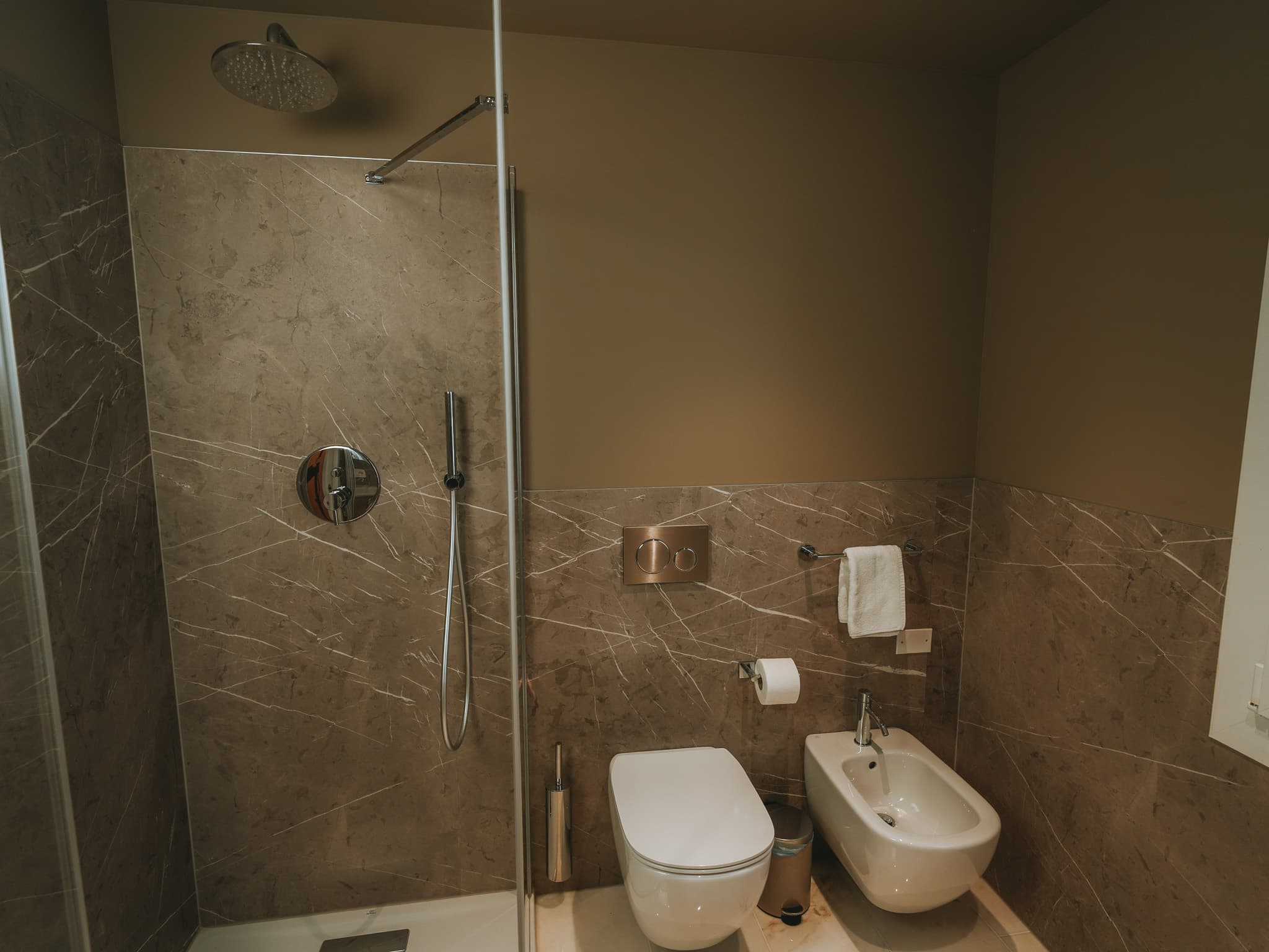 Bagno con doccia a pavimento, soffione tondo, wc e bidet sospesi, rivestimento effetto marmo