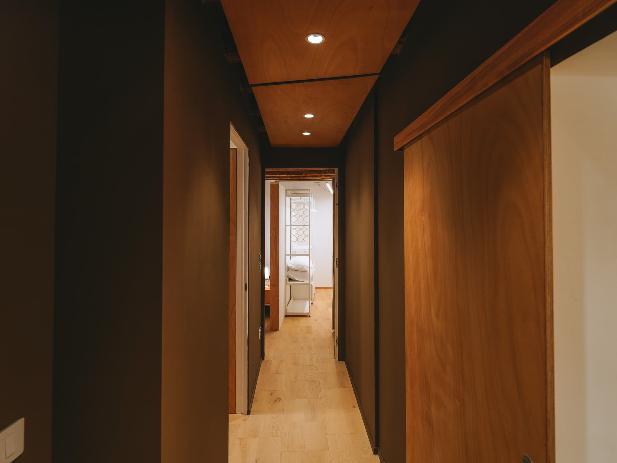 Corridoio con pareti scure, soffitto in legno con faretti e pavimento in parquet chiaro.