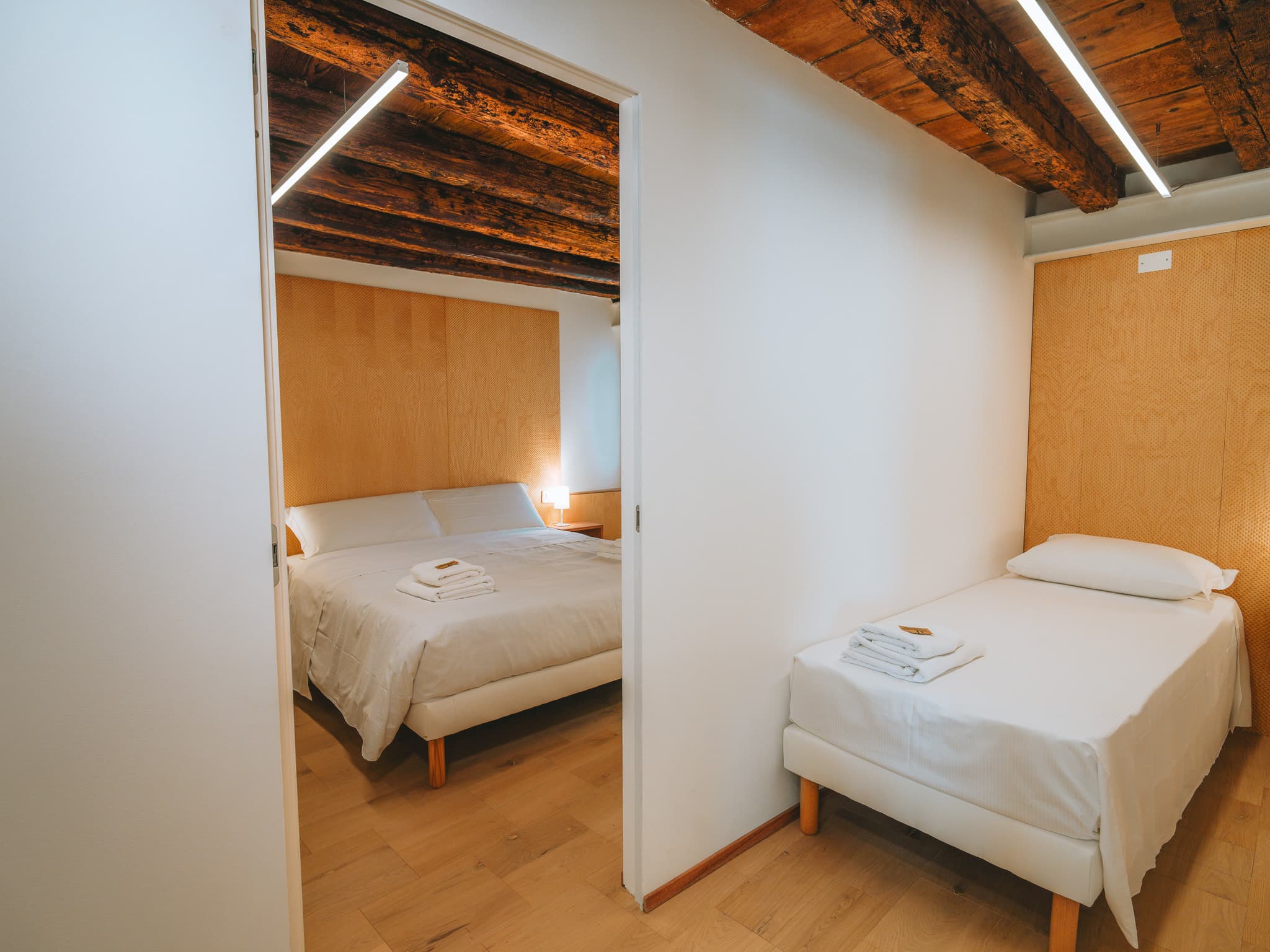 Porta aperta tra la camera con letto matrimoniale e quella con letto singolo, travi a vista.