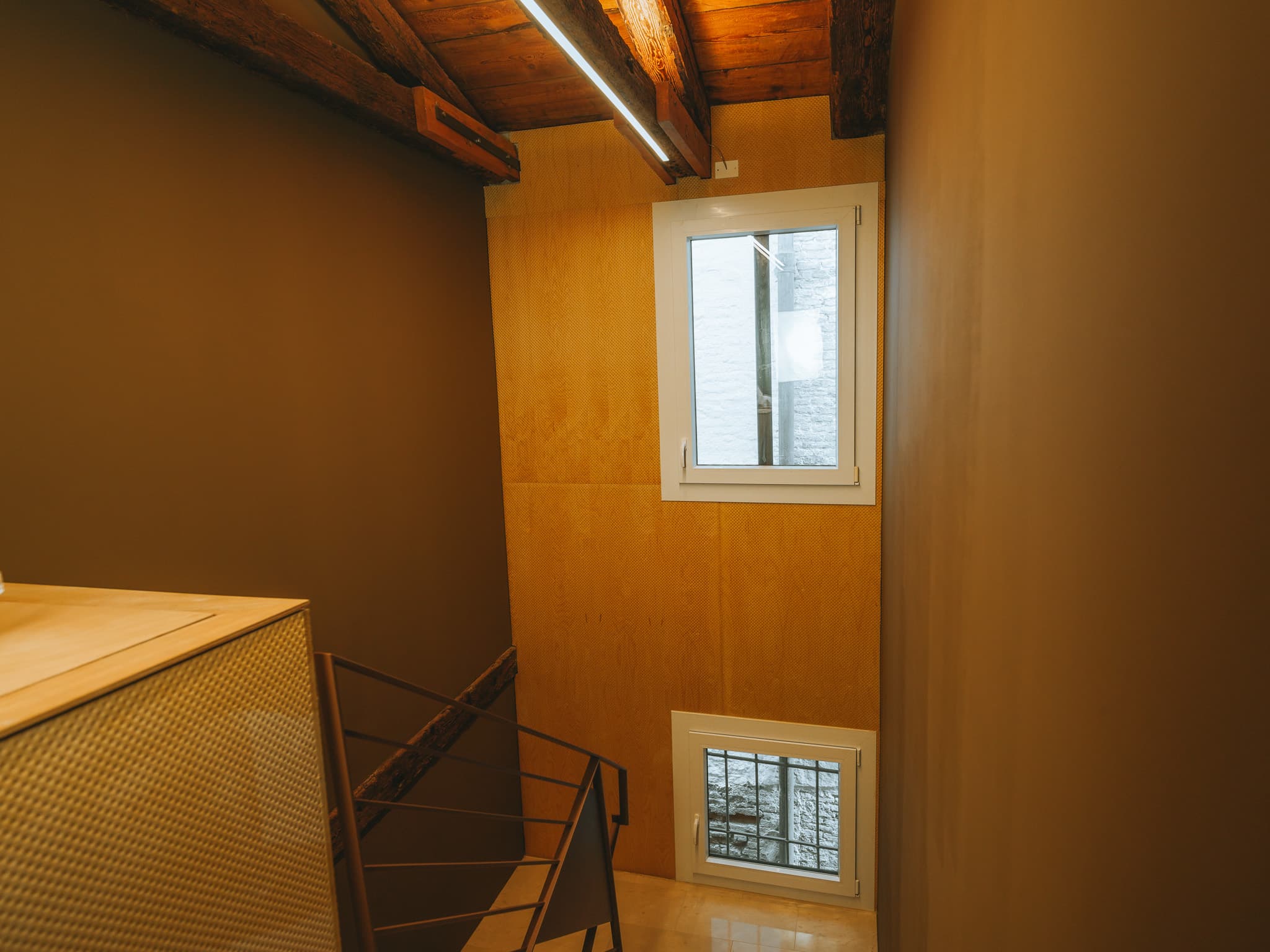 Pianerottolo con travi di legno a vista, due finestre e scala con ringhiera metallica.