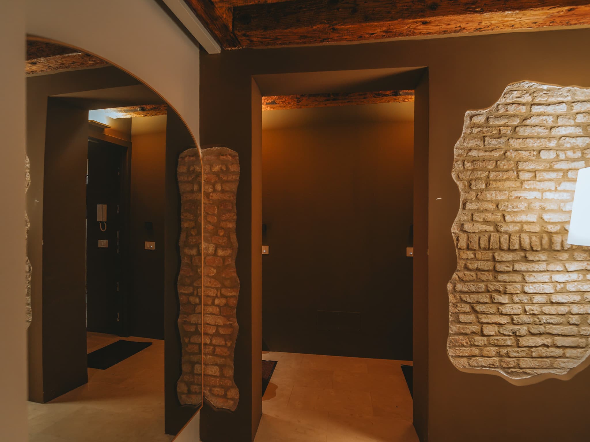 Disimpegno con porzioni di muratura in mattoni lasciate a vista, specchio arcuato e travi di legno.